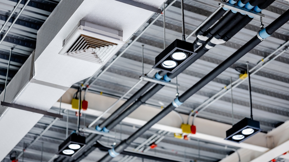 Commercial ceiling fitted with cable trays, electrical conduit, recessed spotlights, and an HVAC air distribution vent